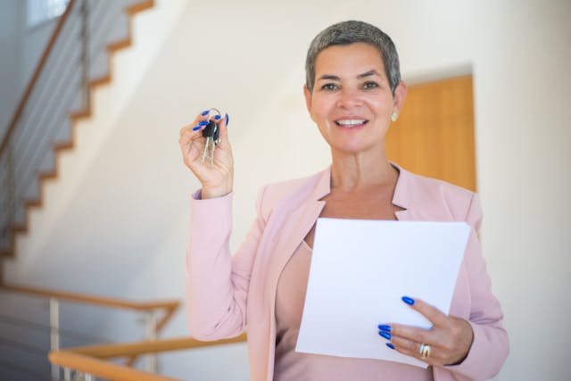 woman-in-pink-blazer-holding-white-paper-and-keys